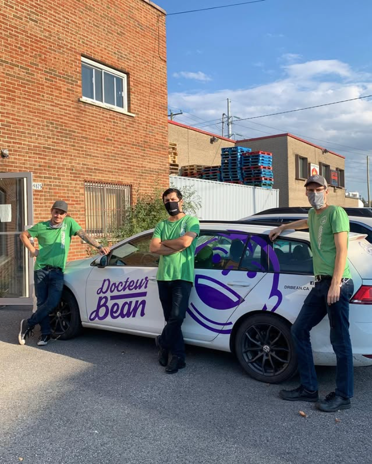 Trois membres de l'équipe en t-shirts verts posant devant une voiture aux couleurs de Docteur Bean
