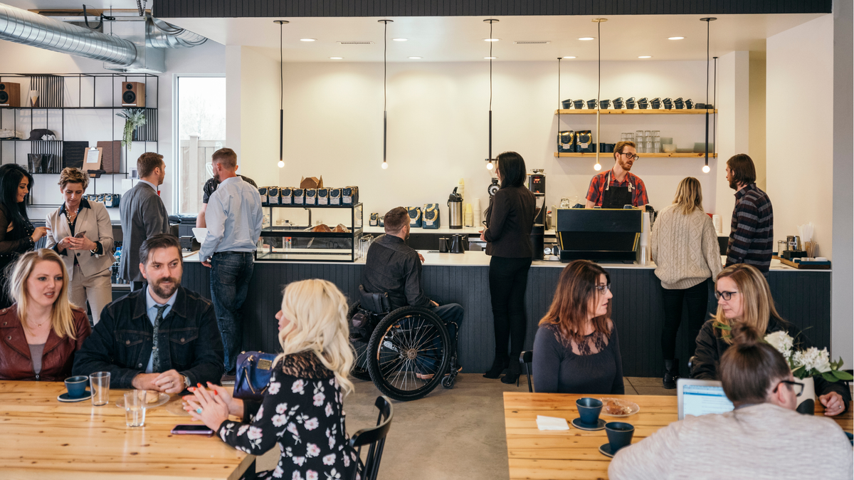 Café achalandé avec clients attablés et barista au comptoir dans un espace moderne et lumineux