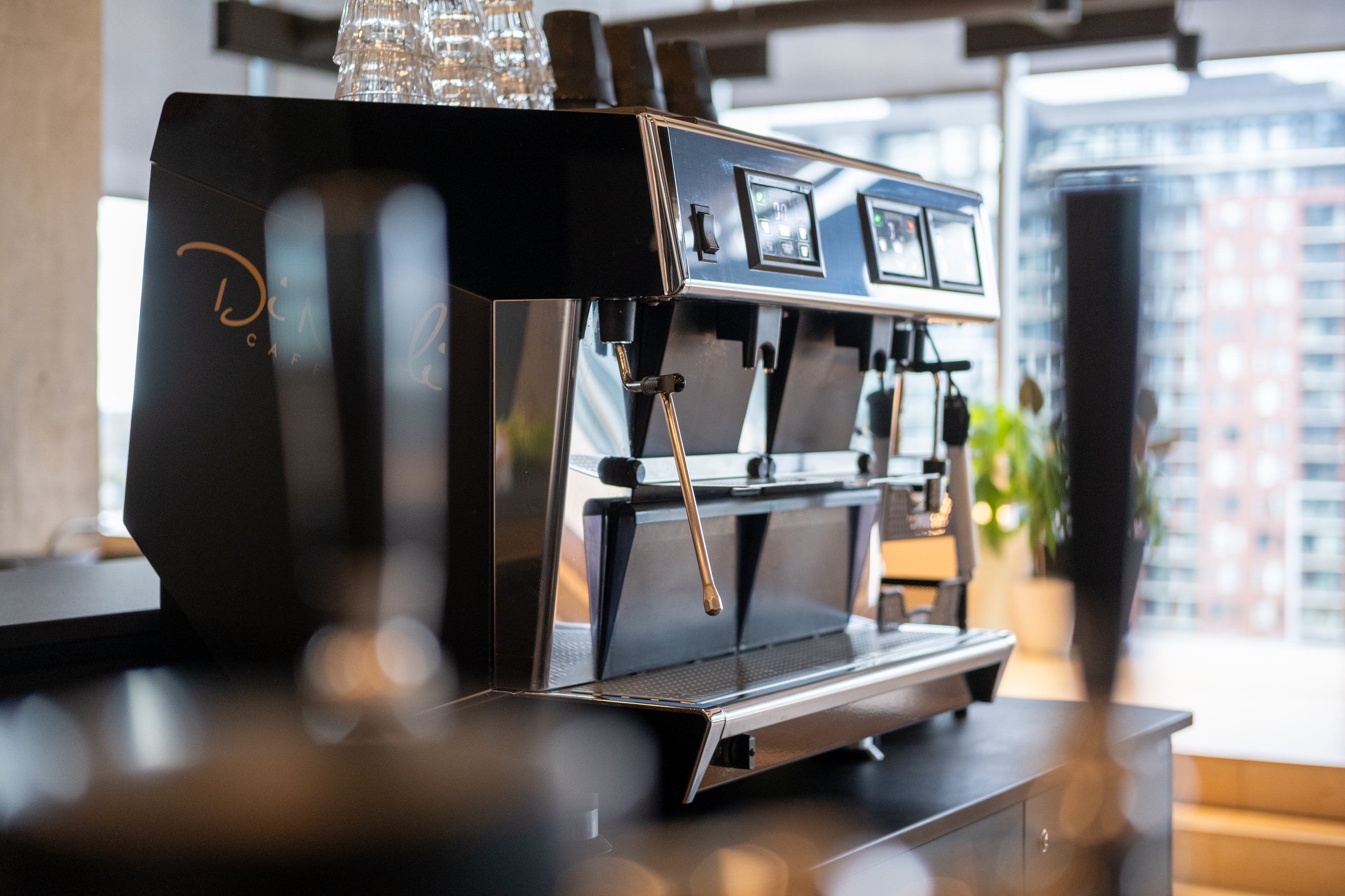Machine à espresso commerciale noire Di Napoli Caffè devant une fenêtre avec vue urbaine