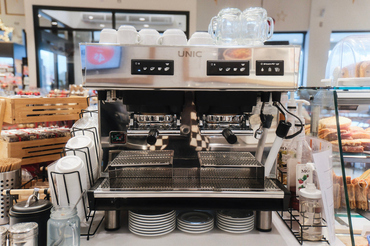 Machine à espresso commerciale UNIC à deux groupes dans un café-épicerie avec tasses empilées