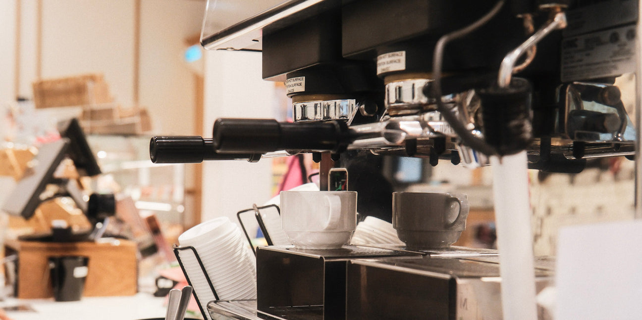 Gros plan des groupes d'une machine à espresso commerciale avec tasses blanches dans un café