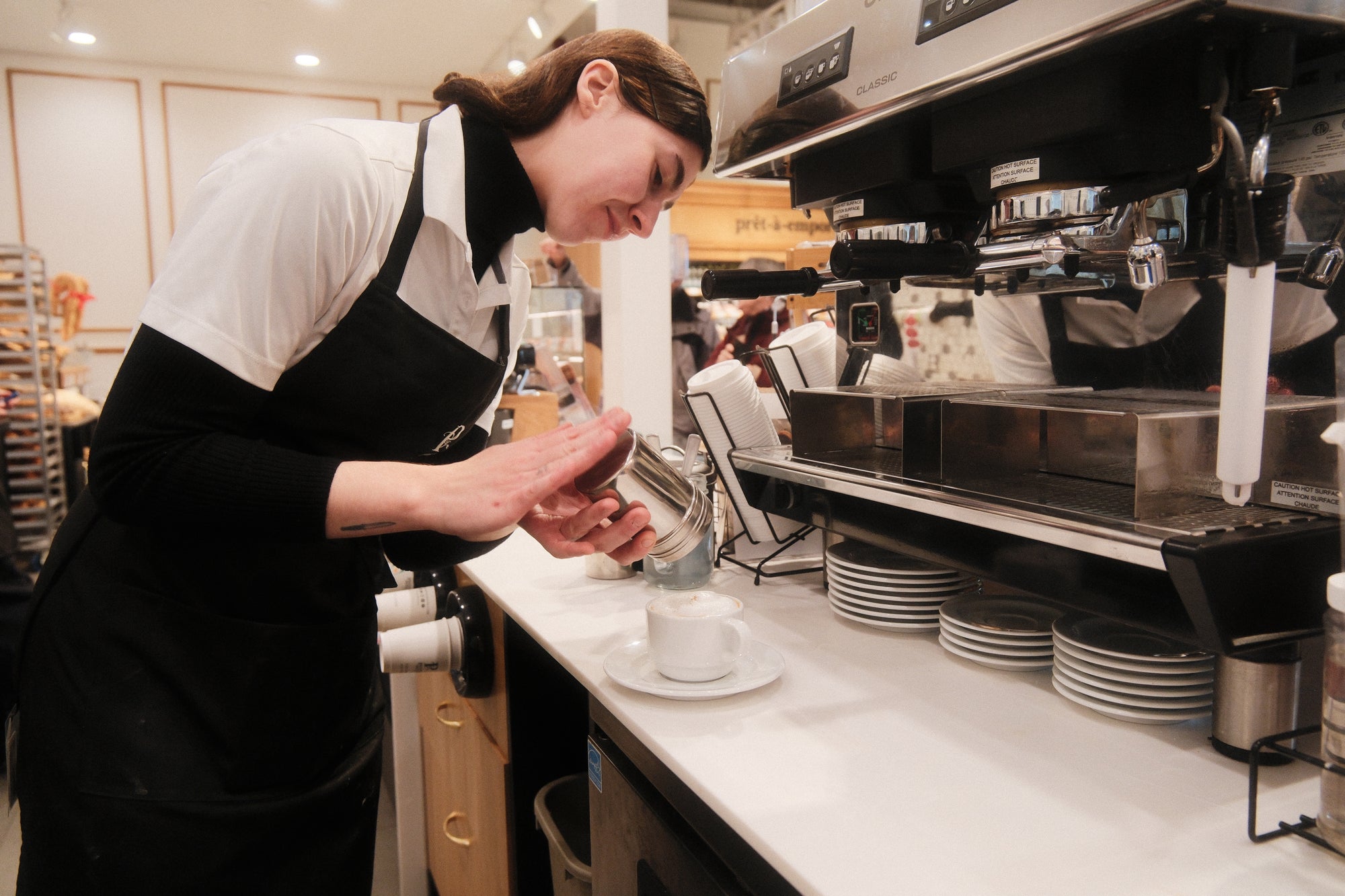 Barista en tablier préparant un café derrière le comptoir d'un café avec une machine à espresso professionnelle
