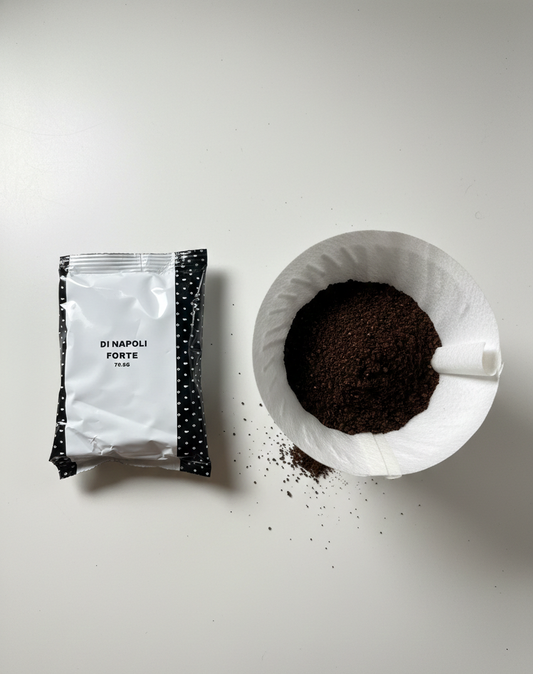 Sachet de café moulu Di Napoli Forte à côté d'une tasse remplie de café moulu, vu de haut