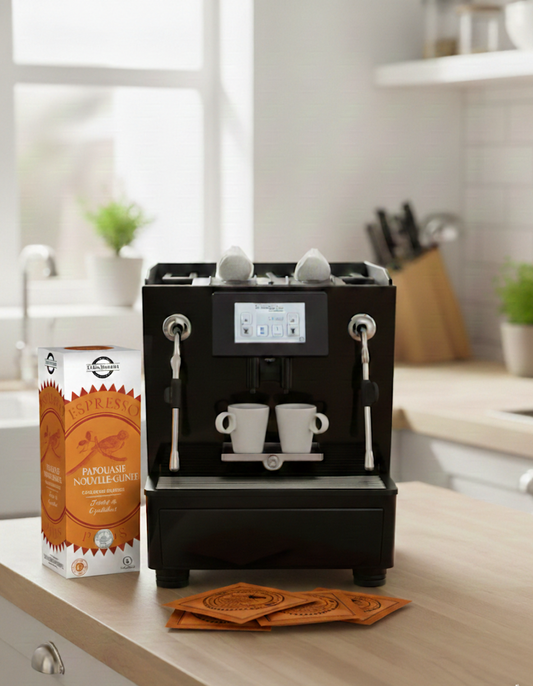 Machine à espresso automatique noire dans une cuisine avec une boîte de café Papouasie-Nouvelle-Guinée et des dosettes