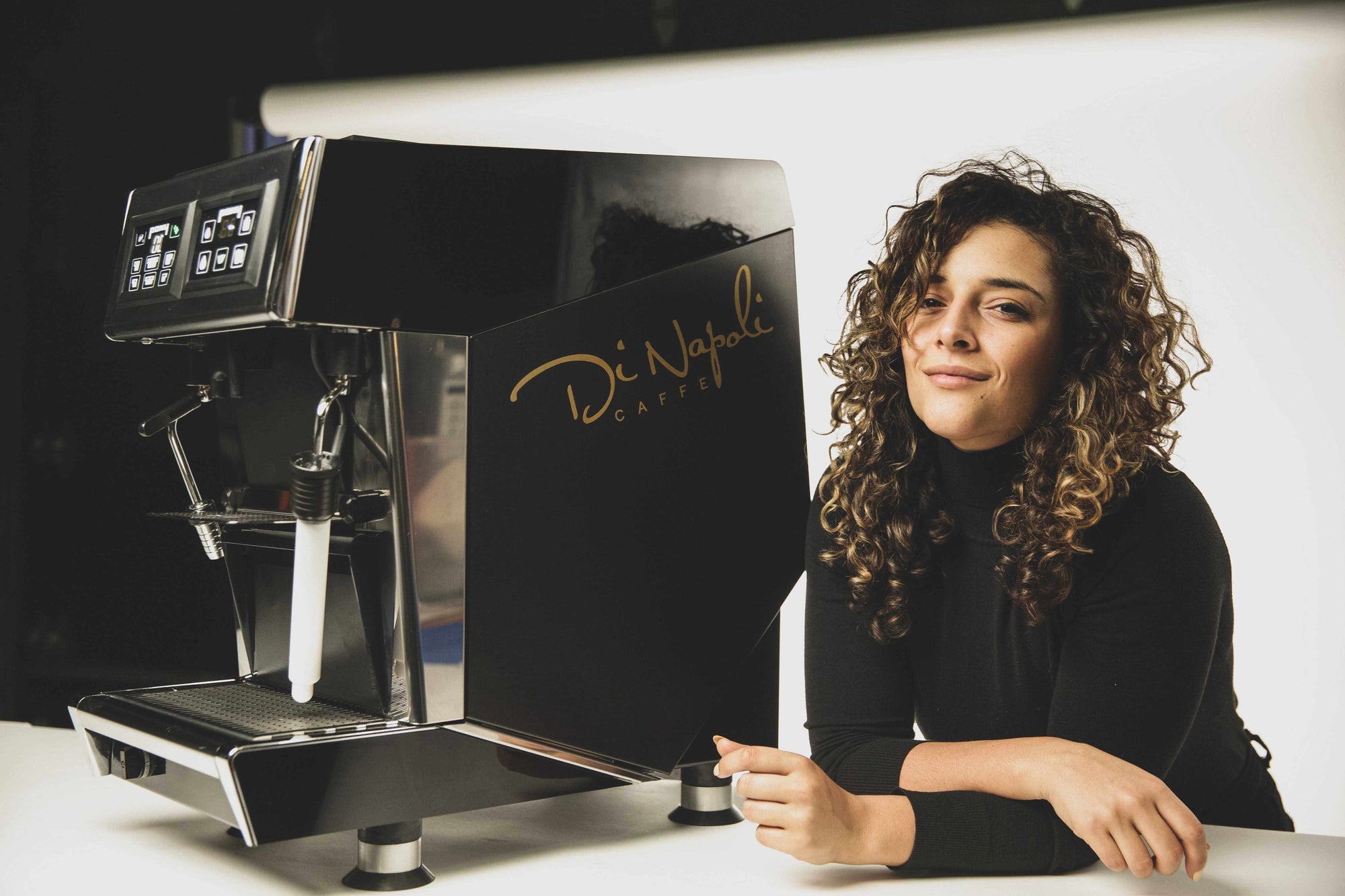 Femme souriante accoudée à côté d'une machine à espresso commerciale Di Napoli Caffè