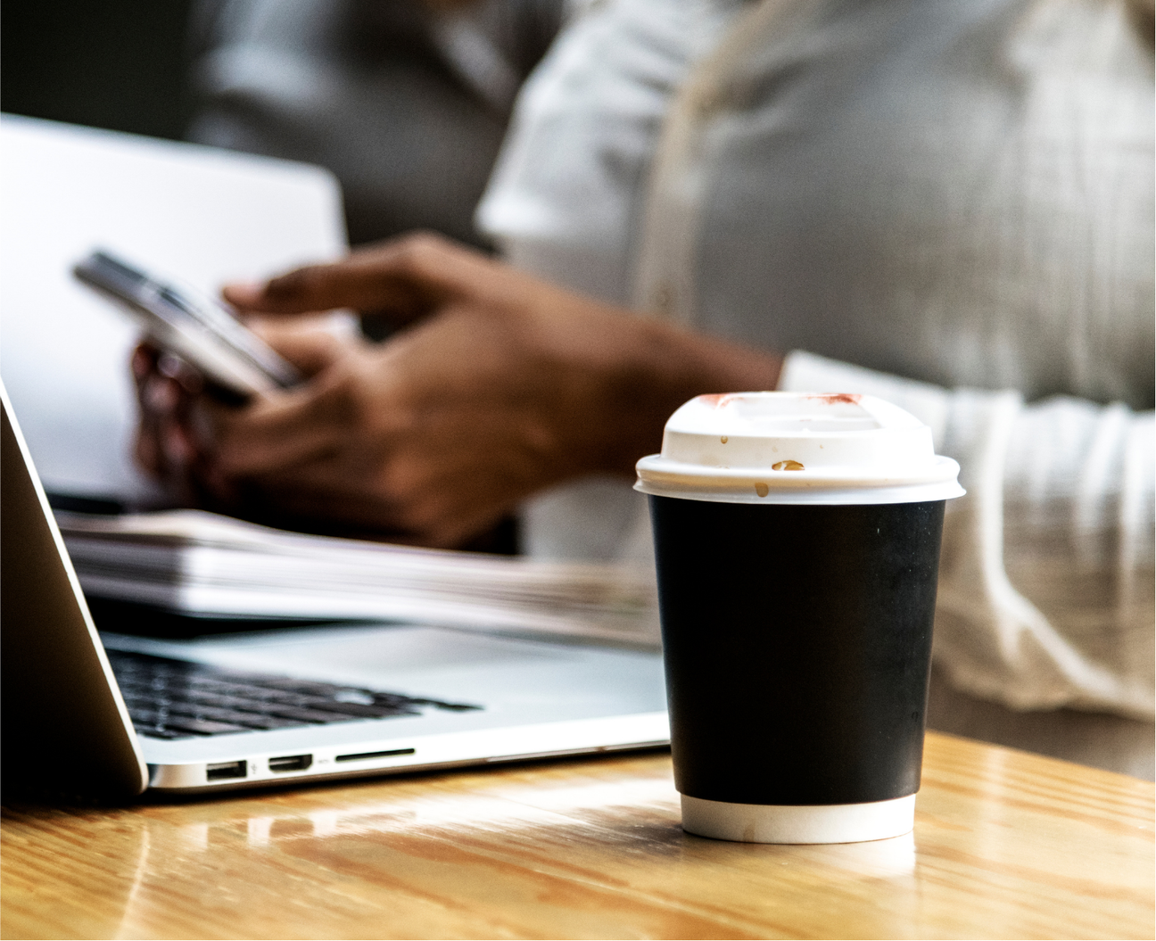 Gobelet de café à emporter sur un bureau pendant qu'une personne utilise un ordinateur portable et un téléphone