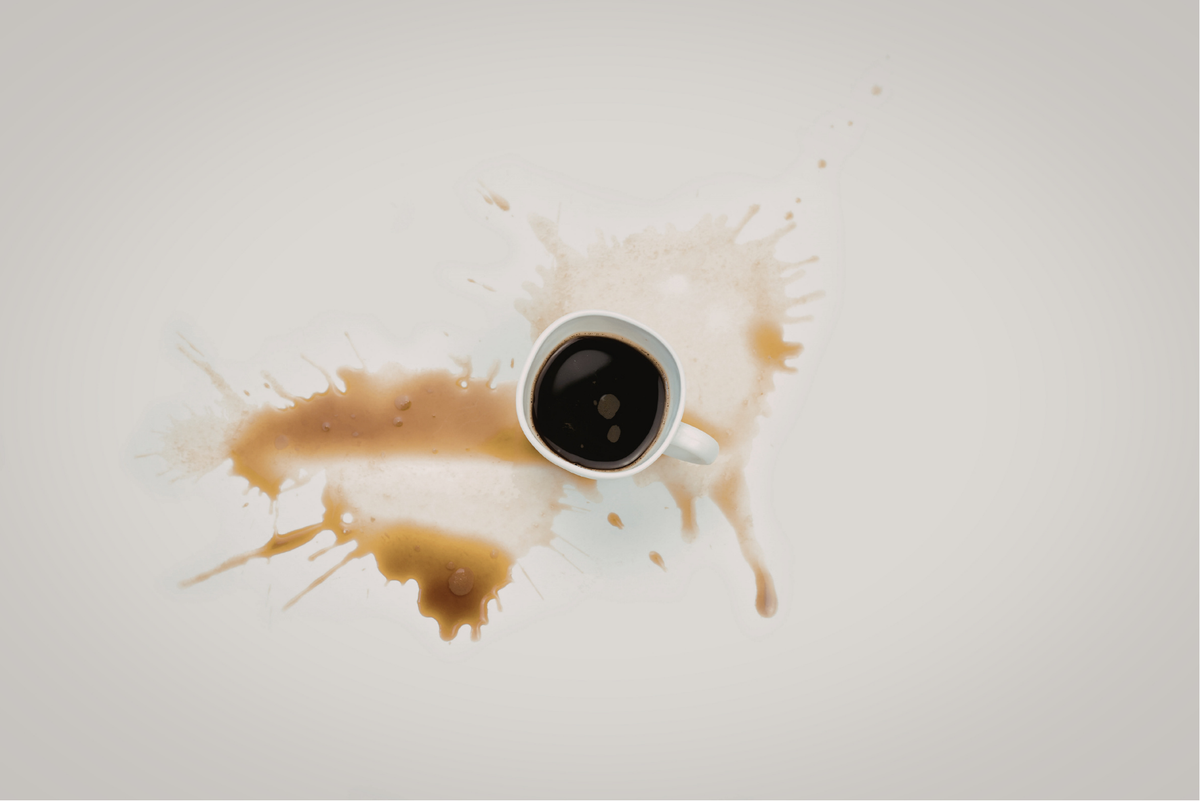 Tasse de café noir renversée laissant une grande éclaboussure de café sur une surface claire